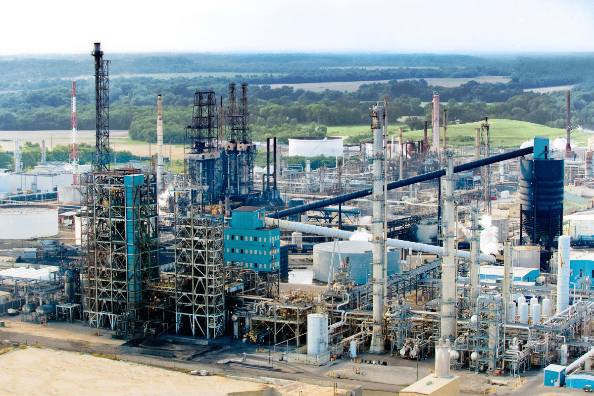 Aerial view of an industrial plant with distillation columns and stacks, surrounded by green farmland